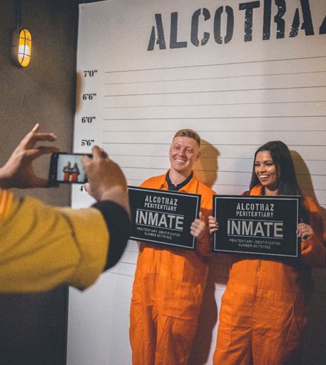 Couple taking mug shot photos at Alcotraz - key part of immersive prison cocktail bar experience.