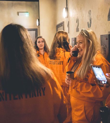 Inmates in orange jumpsuits using prison phones at Alcotraz, the immersive prison-themed bar for fun nights out.