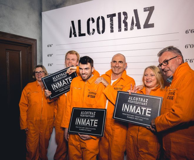 Family in prisoner costumes celebrating at Alcotraz - prison-themed immersive cocktail bar for group activities.