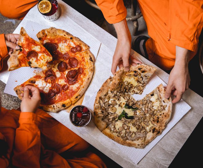 Food service at Alcotraz immersive prison bar - pizza with custom cocktails for a complete night out experience.