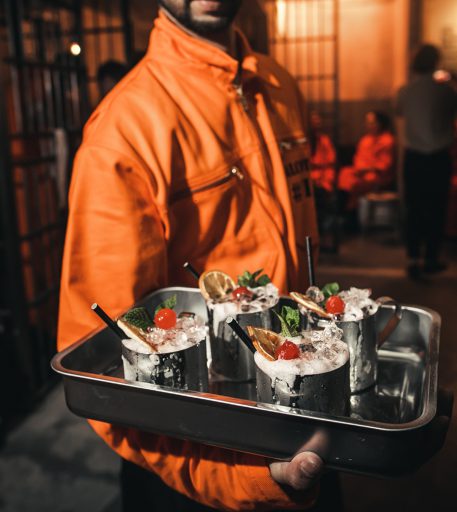 Inmate serving unique canteen cocktails at Brighton Alcotraz - immersive prison bar.