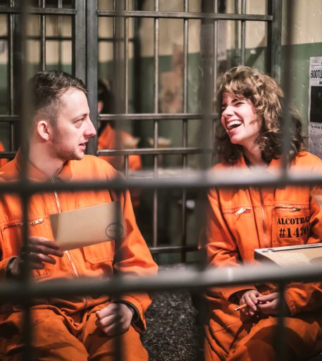 Couple in orange jumpsuits enjoying cocktails at Brighton Alcotraz - immersive prison-themed bar.