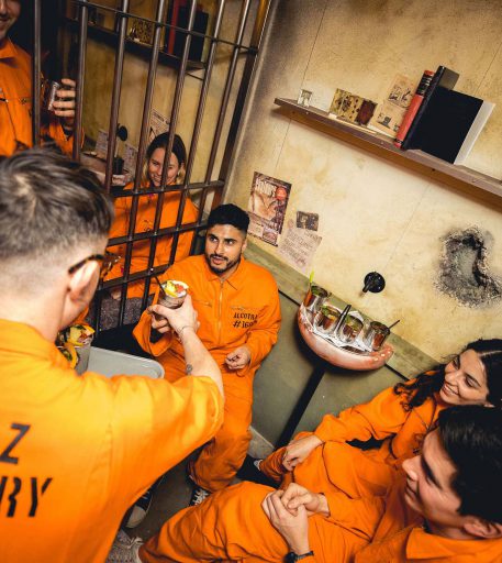 Inmates enjoying cocktails behind bars at Alcotraz - immersive prison bar experience for fun nights out.