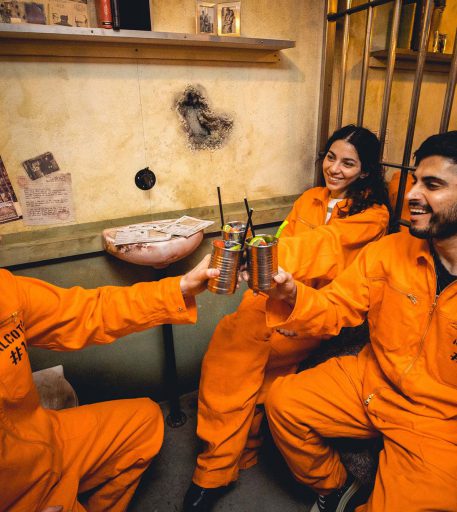 Inmates in orange jumpsuits enjoying Christmas cocktails at Alcotraz - immersive prison bar.