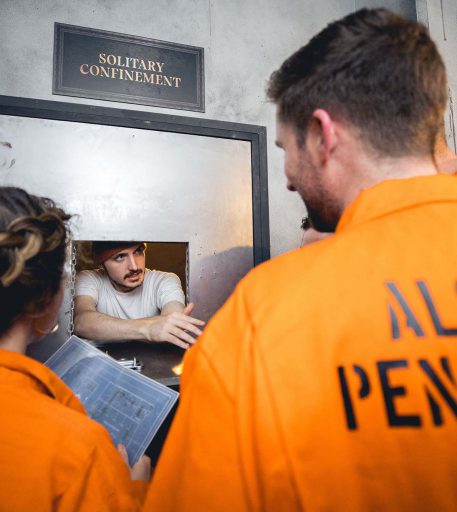 Customers in orange jumpsuits interacting with prisoner character - interactive cocktail bar in prison setting.