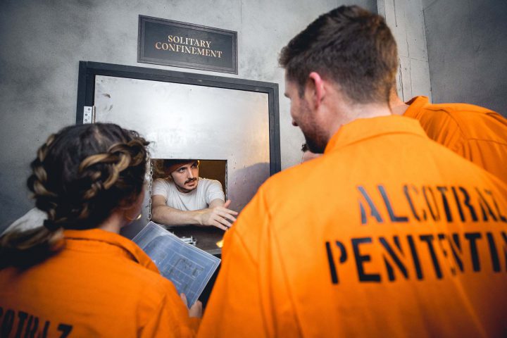 Customers in orange jumpsuits interacting with prisoner character - interactive cocktail bar in prison setting.