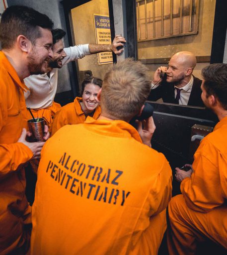 Inmates in orange jumpsuits interacting with prison guard character - interactive prison-themed bar experience.
