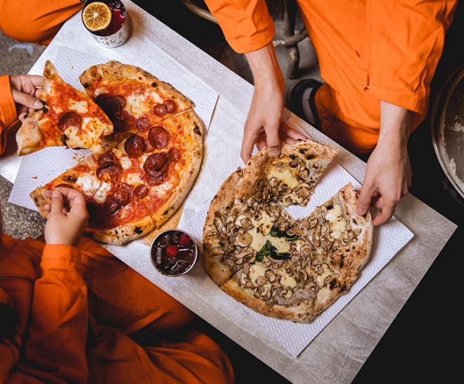 Food service at Alcotraz immersive prison bar - pizza with custom cocktails for a complete night out experience.