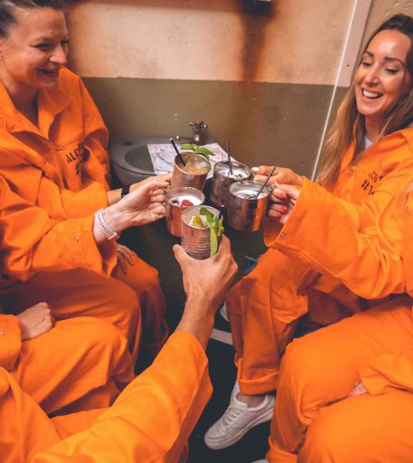 Inmates in orange jumpsuits enjoying cocktails at Alcotraz - immersive prison bar experience popular for hen nights