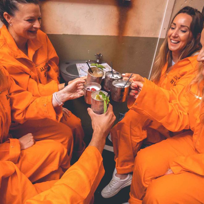 Inmates in orange jumpsuits enjoying cocktails at Alcotraz - immersive prison bar experience popular for hen nights