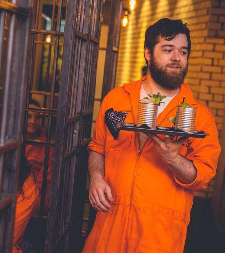 Inmate character serving custom cocktails at Alcotraz - prison bar immersive experience.