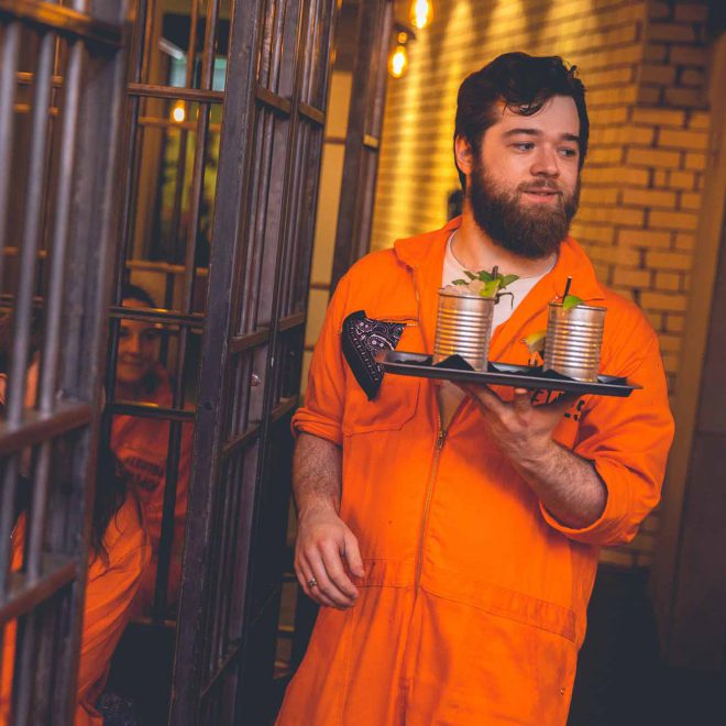 Inmate character serving custom cocktails at Alcotraz - prison bar immersive experience.