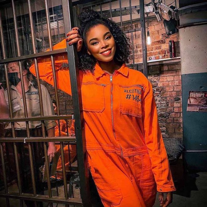Customer in orange jumpsuit enjoying cocktails at Alcotraz - immersive prison bar experience.