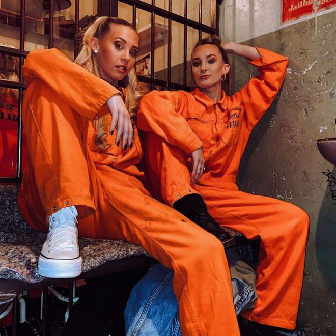 Friends in orange jumpsuits enjoying cocktails at Alcotraz - cocktail bar in immersive prison setting.