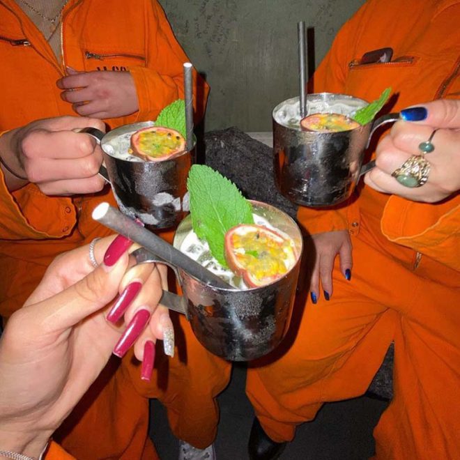 Inmates enjoying cocktails with fruit garnish at Alcotraz - premium drink from this immersive prison bar.