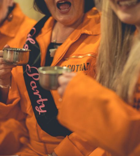 Hen party inmates with cocktails at Alcotraz - immersive prison-themed cocktail bar experience with theatrical elements.