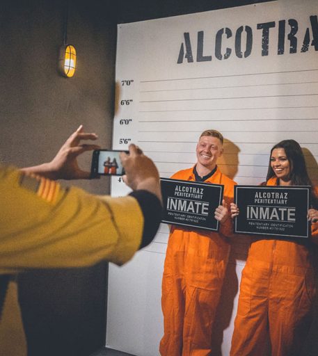 Couple taking mug shot photos during date night at Alcotraz - interactive element of this immersive prison bar experience.