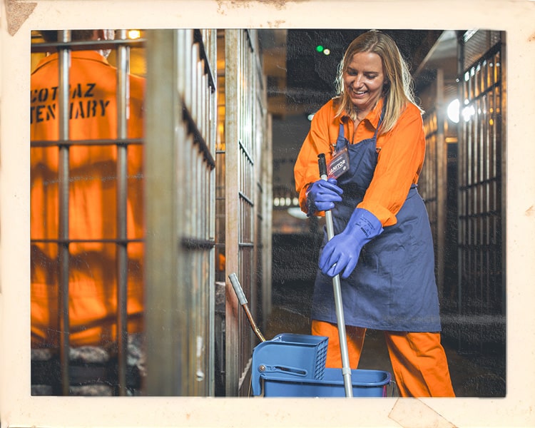 Customer in orange jumpsuit working as cleaner at Alcotraz immersive experience - interactive prison-themed cocktail bar.